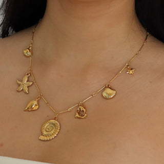 Woman wearing a gold necklace with various pendants on a plain background
